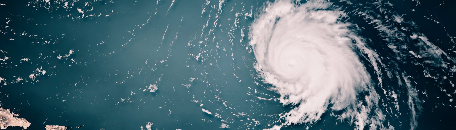 Satellite view of a hurricane with a visible eye and spiral cloud bands over the Atlantic Ocean, with Caribbean islands at the lower left.